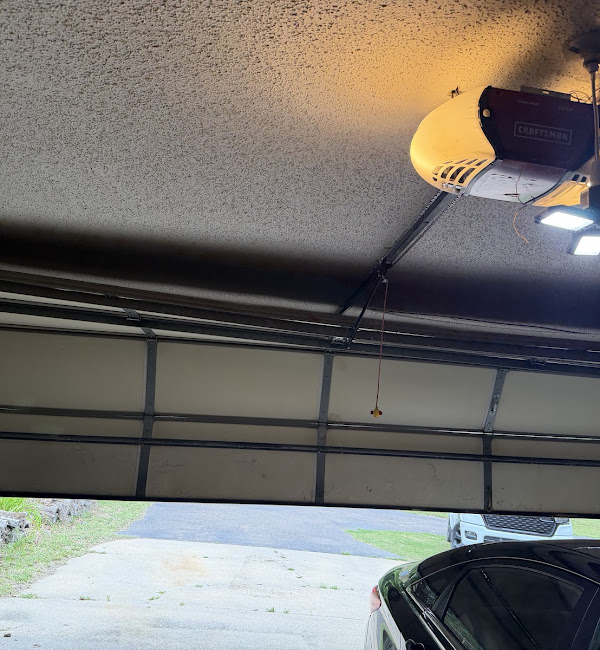 Ceiling-mounted garage door opener above a partly open residential garage door