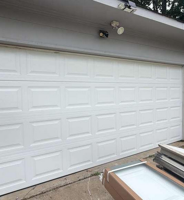 White residential garage door with new door sections and installation materials visible nearby